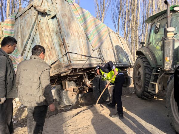 沙雅县央塔克协海尔乡派出所民警手持工具，蹲在拖车车轮旁，将松软地面垫平。他专注地调整着垫土的厚度与平整度，给拖车脱困创造最佳条件，保障拖拽过程万无一失。.jpg